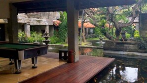 A pool table in a covered area with a view of a garden and a pond. - Grand Balisani Suites Hotel (Keroboken Kelod)