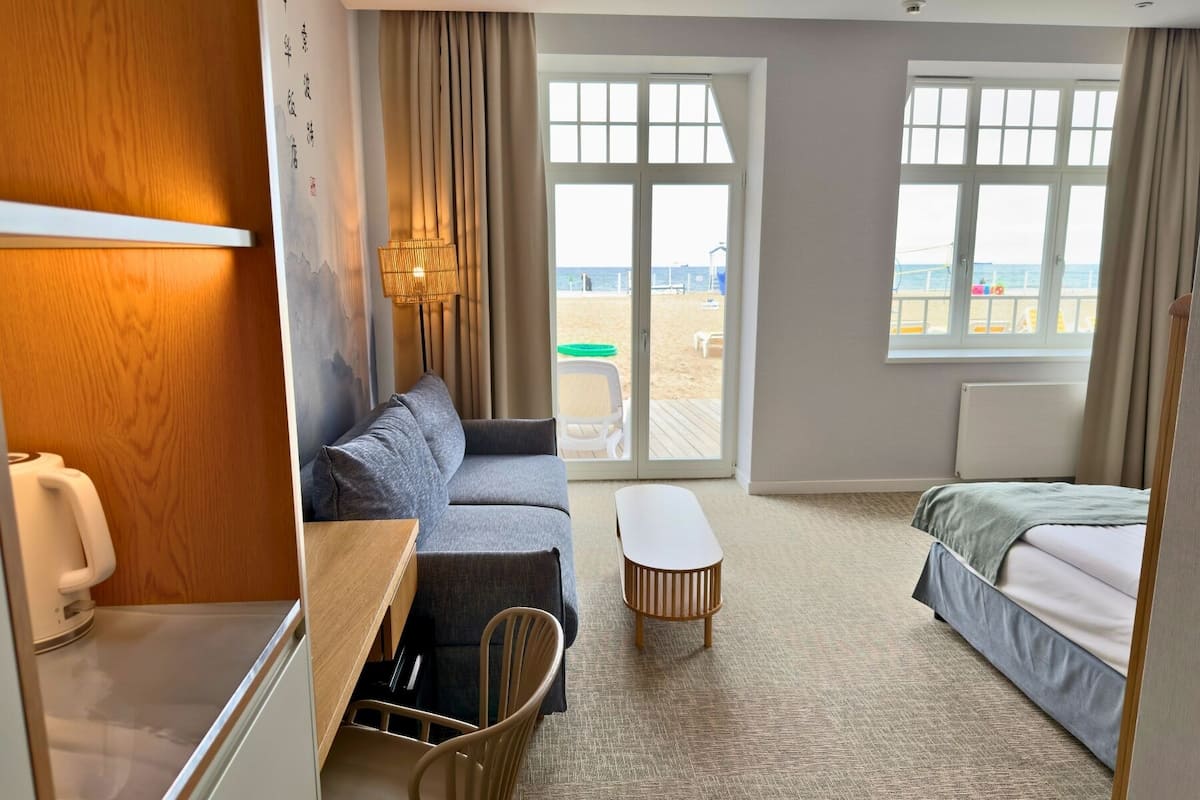 Habitación de hotel con sofá, cama, una mesita y vistas a la playa a través de amplias ventanas.