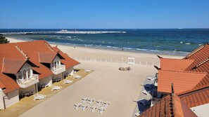 Un hôtel situé en bord de mer, doté d’une terrasse en bois et de chaises longues, avec une jetée en arrière-plan et une vue dégagée sur l’océan.