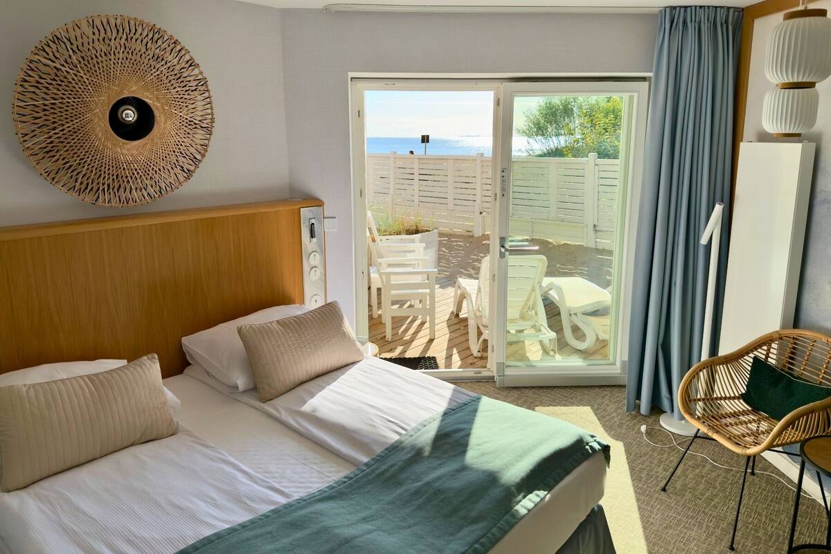 Una habitación de hotel con una cama, un sillón de mimbre y vistas al área exterior.