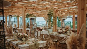 Un área de comedor al aire libre con pérgolas de madera, sillas de mimbre y mesas dispuestas para una comida.
