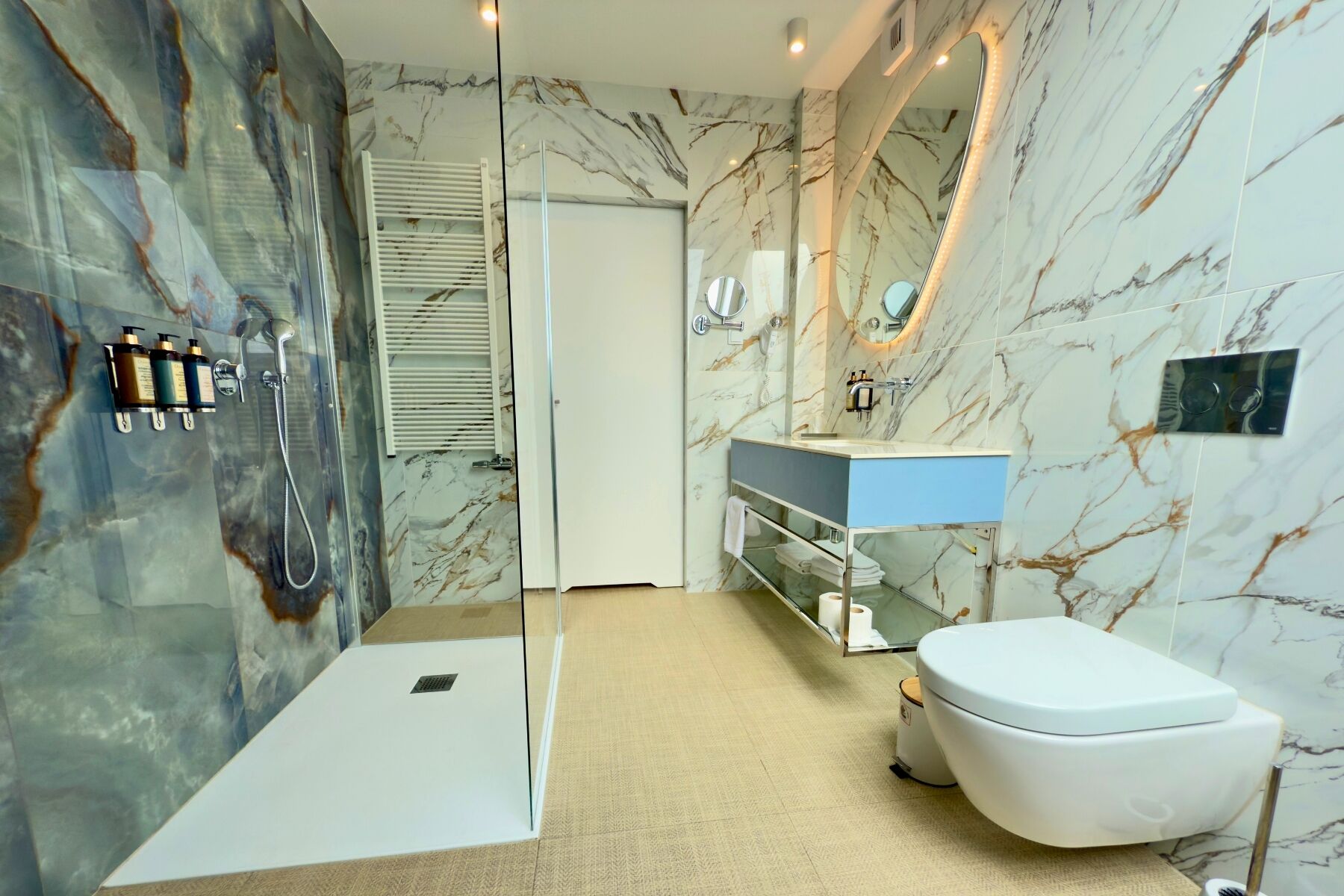 A modern bathroom with a glass shower enclosure, a white toilet, and a vanity with a marble backsplash.
