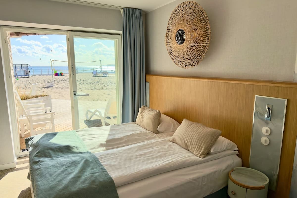Habitación de hotel con una cama grande, cabecera de madera, un adorno en la pared y vista a la playa a través de una puerta corrediza.