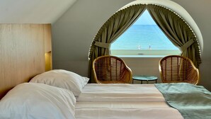 Un dormitorio con cama, dos sillones de mimbre, una mesita y vista al mar.