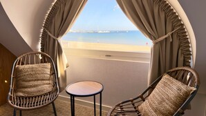 Un balcón con sillas de mimbre y una mesita pequeña, con vista a una playa y un muelle.