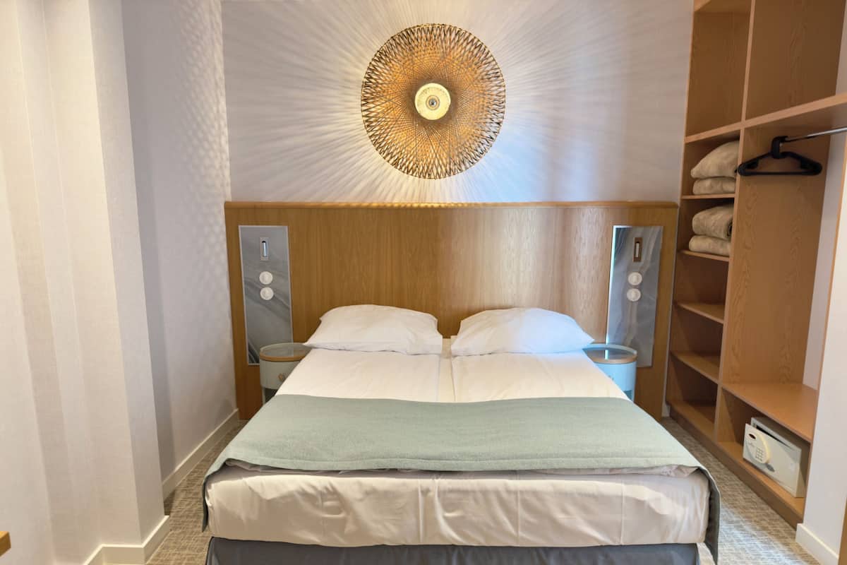 Habitación de hotel con cama, mesitas de noche, un espejo, un armario y una lámpara de techo original.