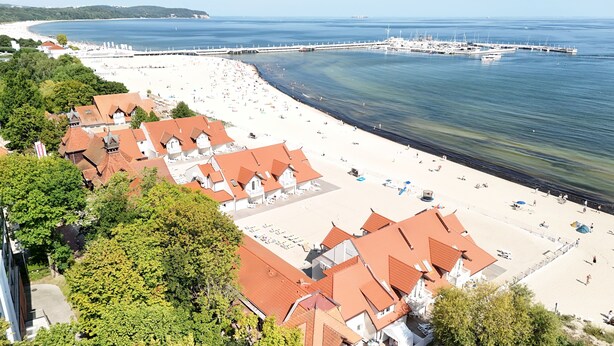 Un hotel costero con techos de tejas rojas, una playa y un muelle.