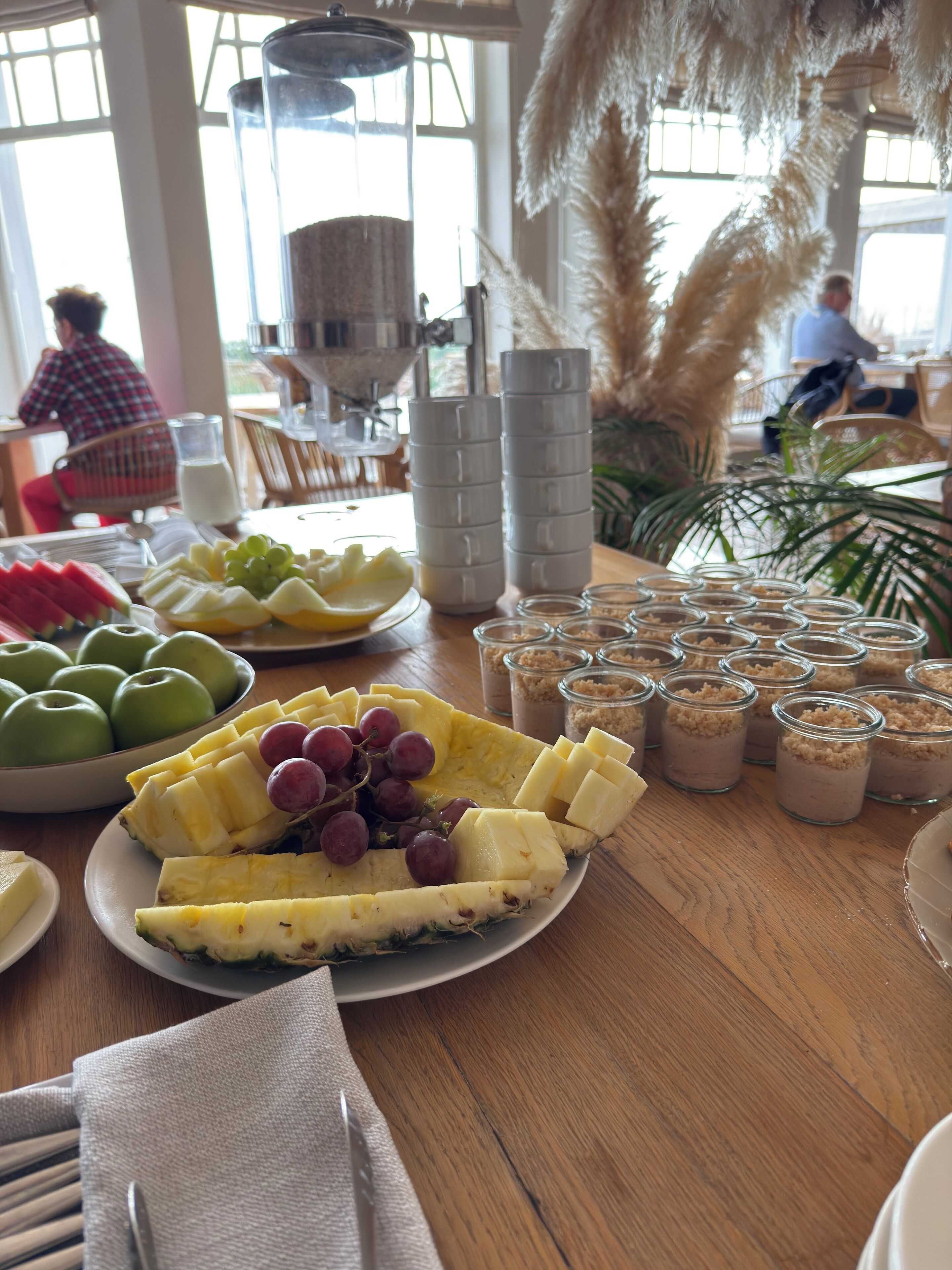 A breakfast buffet with various fruits, a coffee machine, and small jars of food.