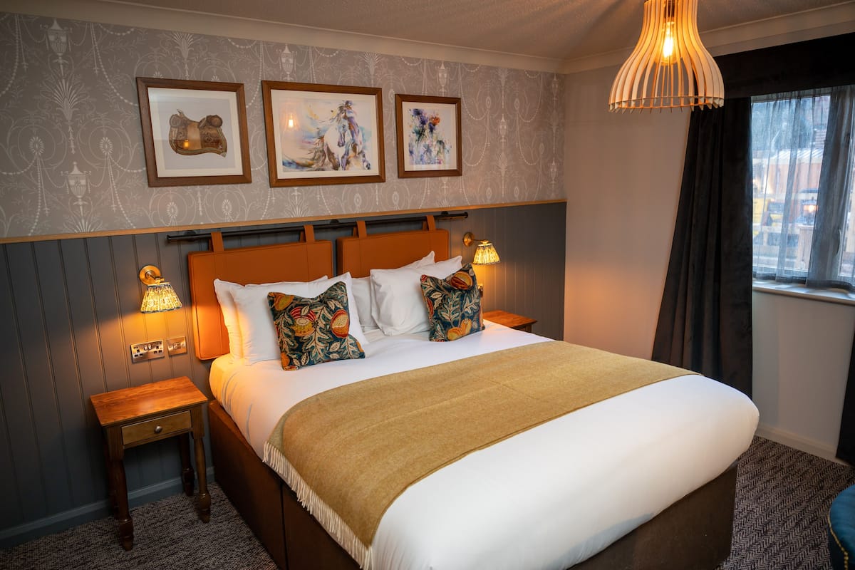 A neatly made bed with a brown blanket, two bedside tables with lamps, and three framed artworks on the wall.