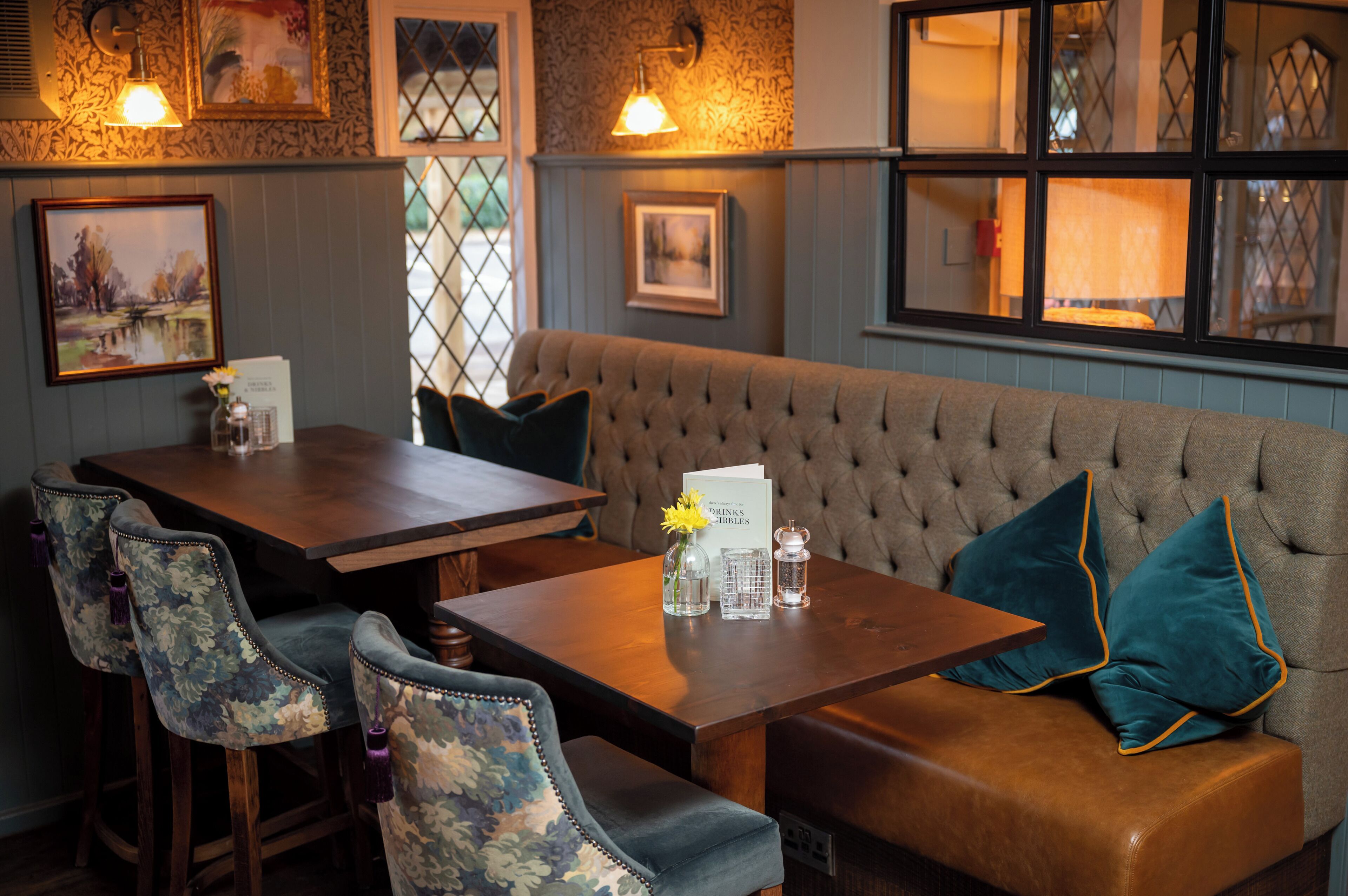 A cozy seating area with a cushioned bench and a wooden table, featuring floral-patterned chairs and a menu sign.