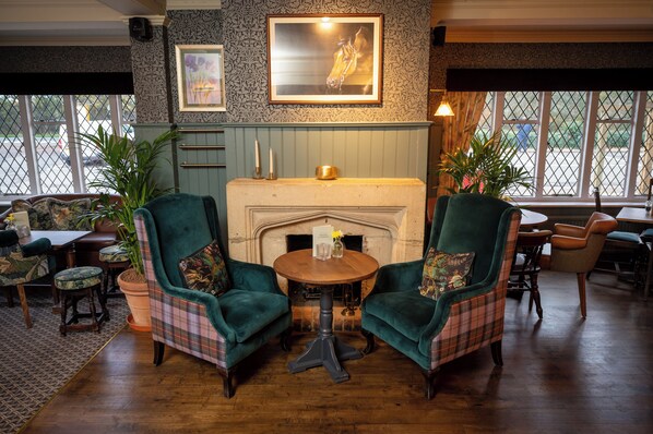 A cozy room with two plush armchairs, a wooden table, and a fireplace.