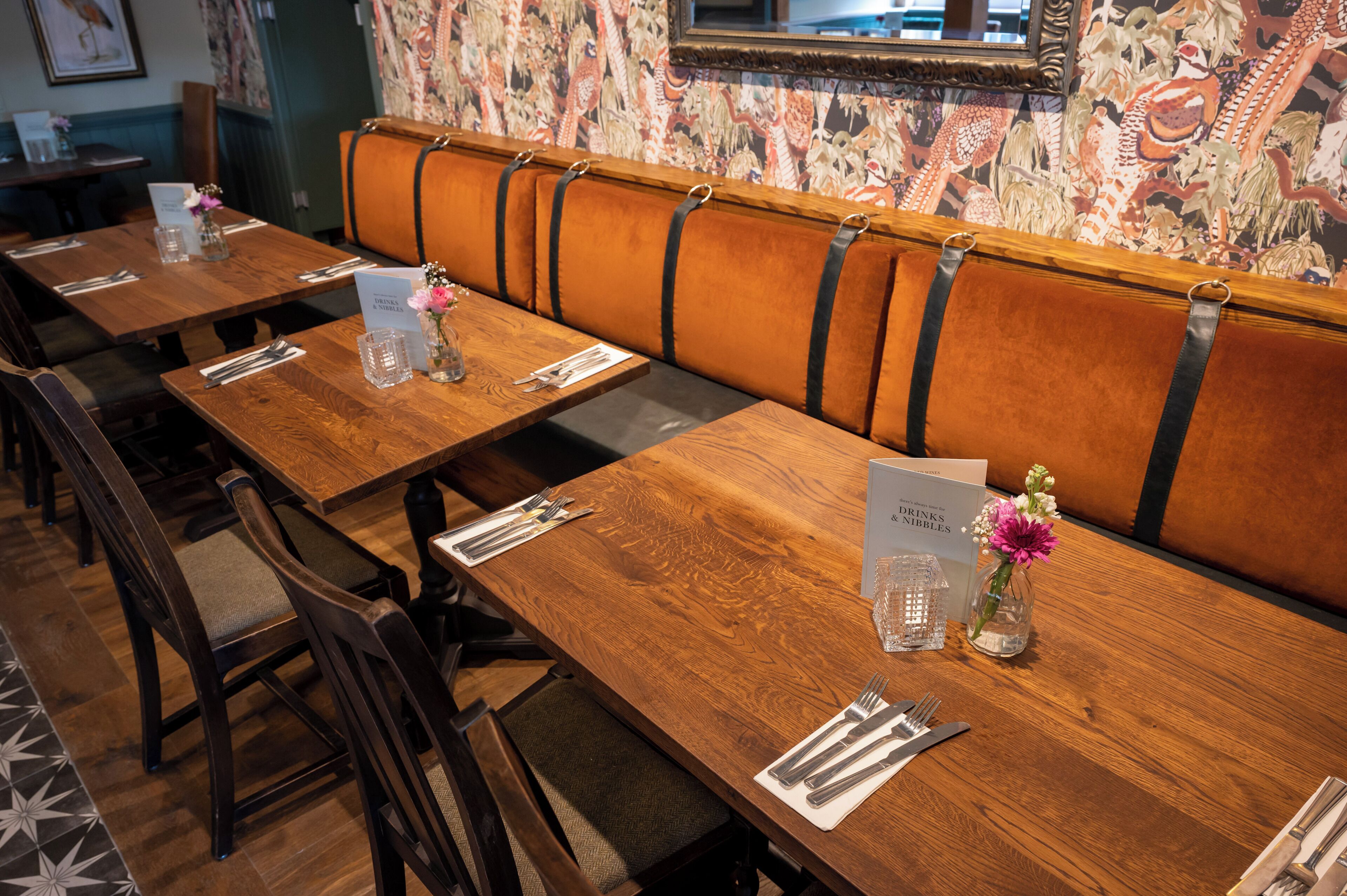 A restaurant with wooden tables and cushioned booths, each with a menu and a glass of water.