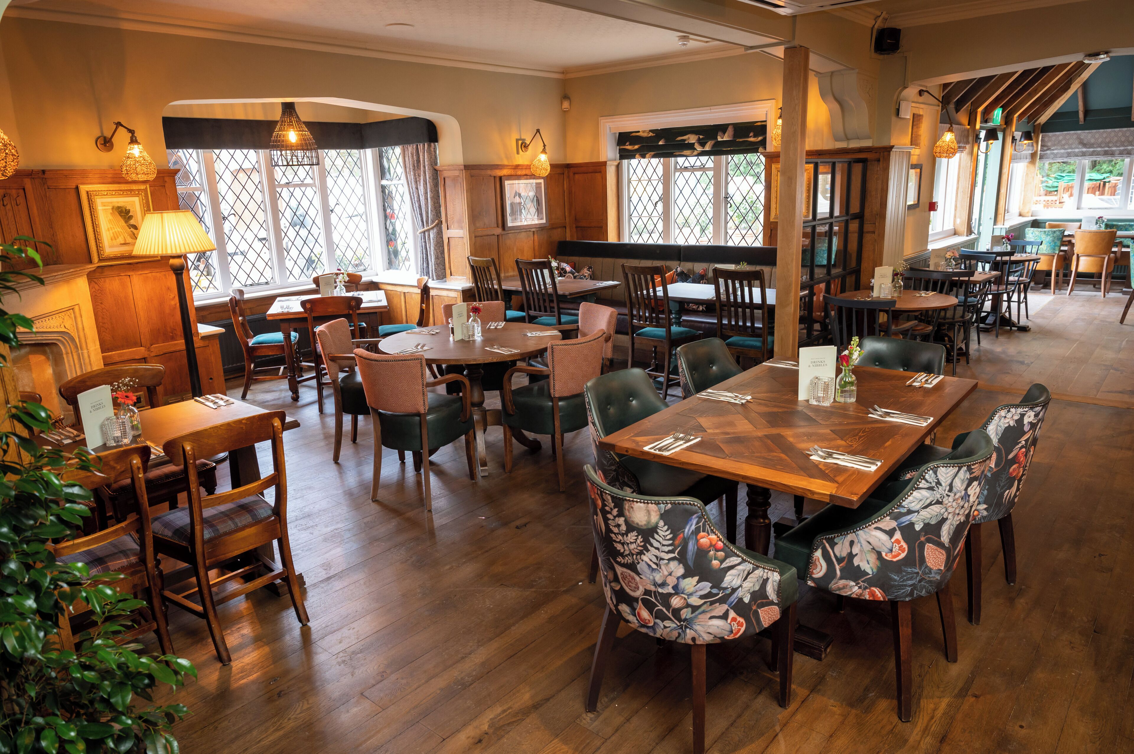 Un restaurante con mesas y sillas de madera, una chimenea y ventanas amplias con cortinas.