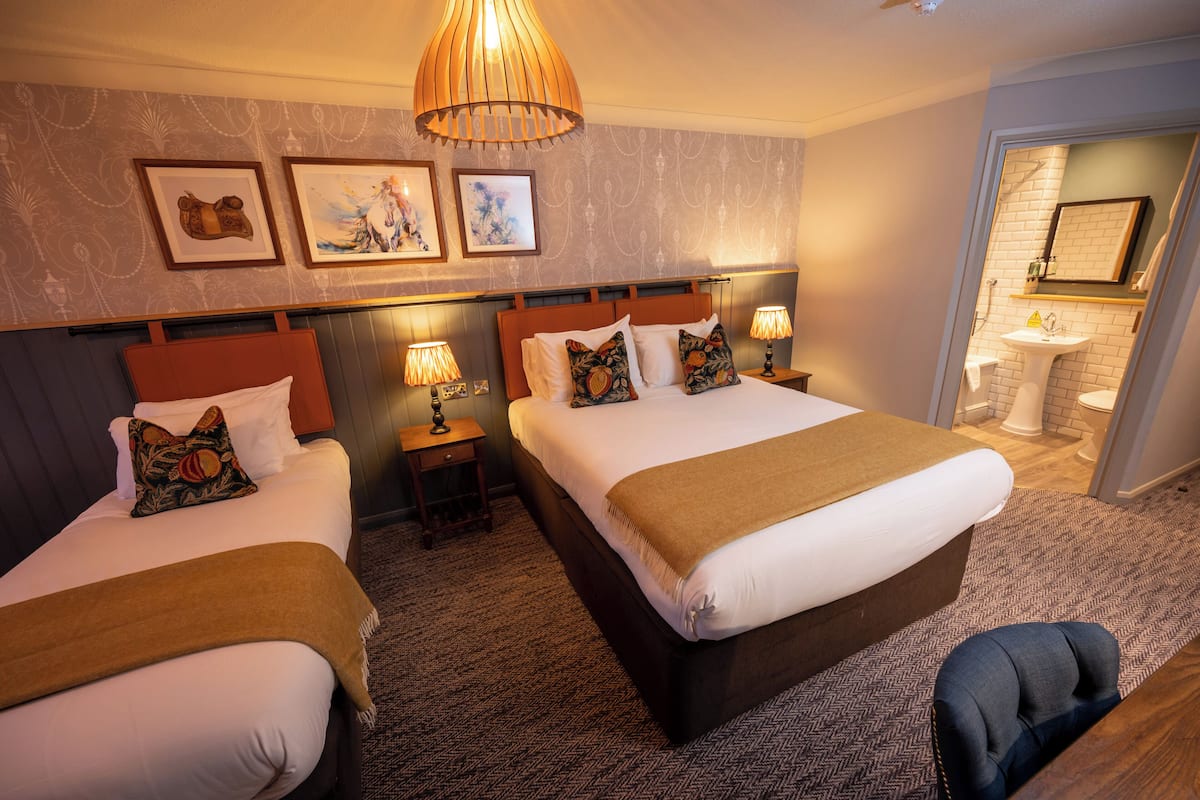 A hotel room with two beds, a wooden headboard, a large window, and a bathroom visible through an open door.