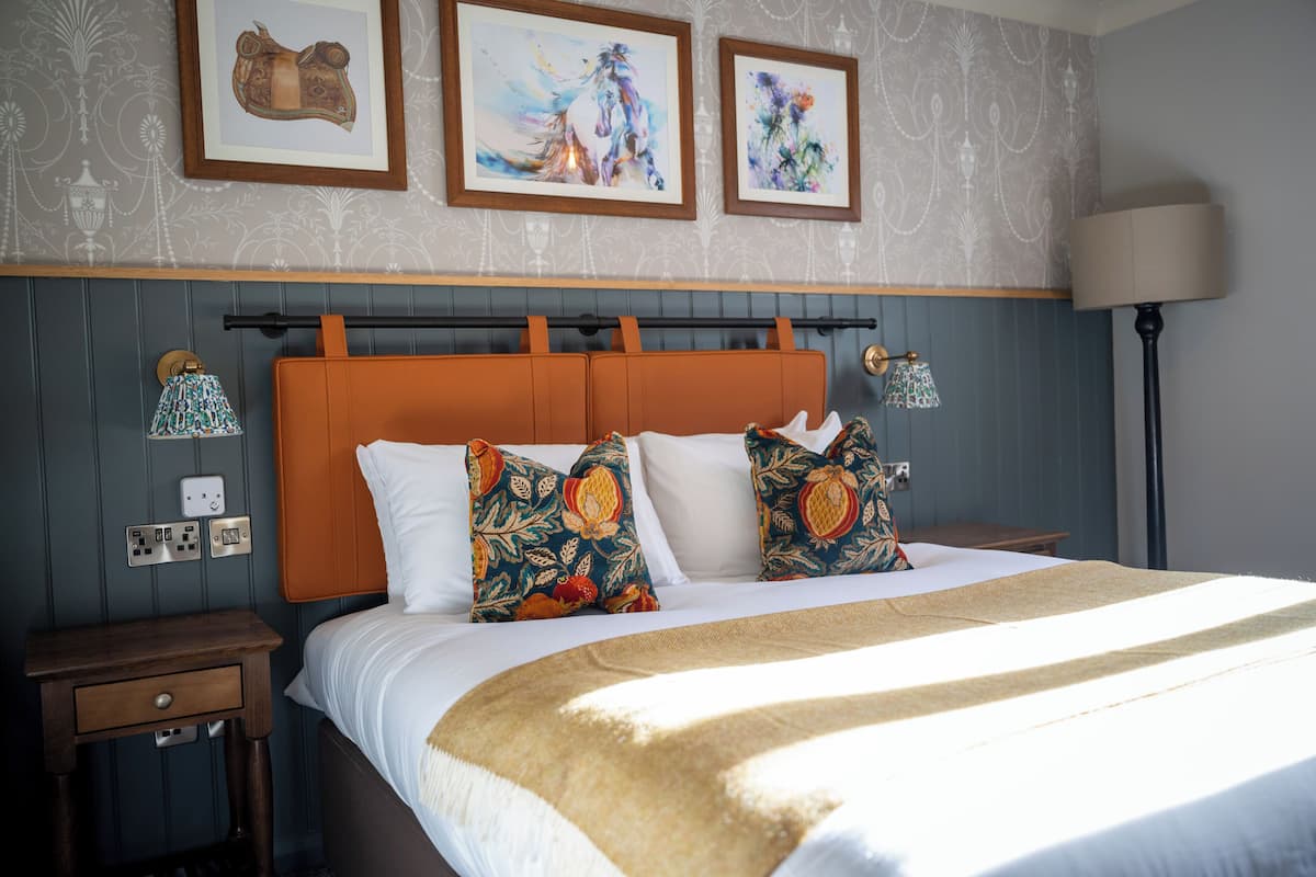 A neatly made bed with a patterned headboard, a bedside table with a lamp, and framed artwork on the wall.
