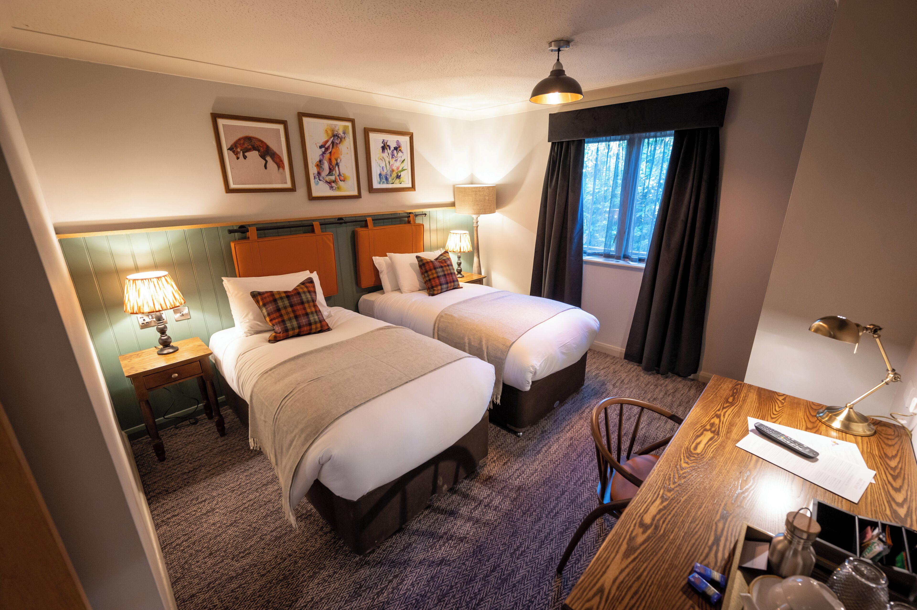 Une chambre d’hôtel avec deux lits, un bureau, une chaise, une lampe et des œuvres d’art accrochées au mur.