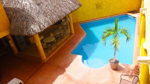 A pool area with a thatched roof seating area and a palm tree. - Villas La Lupita (Acapulco)