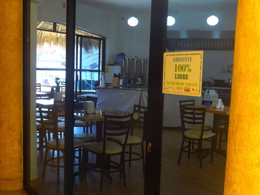 A restaurant with a glass door, interior seating, and a kitchen visible through the door.