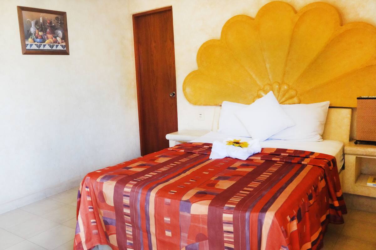 Una habitación con una cama, una puerta de madera, un cuadro en la pared y un cabecero grande y decorativo.