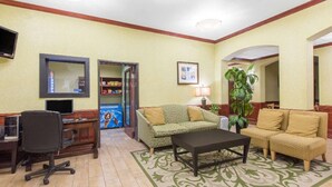Un vestíbulo de hotel con una mesa de recepción, un sofá verde, un sofá amarillo, una mesa de centro, un televisor y una planta.