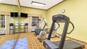 Un gimnasio con equipo de ejercicio, un reloj y una ventana con cortinas.