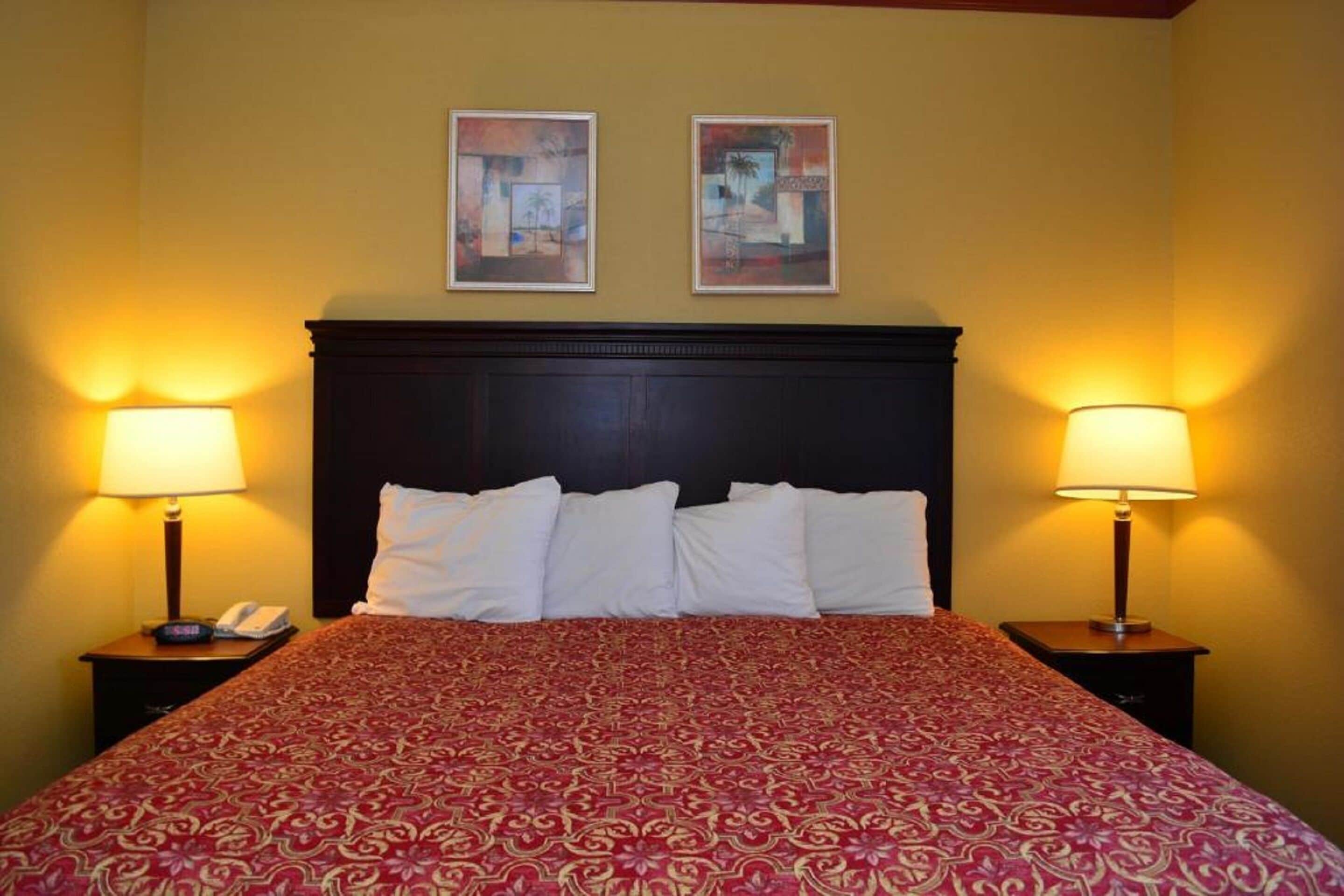 Une chambre d’hôtel avec un grand lit, deux lampes de chevet, une tête de lit sombre et deux œuvres d’art encadrées accrochées au mur.