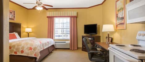 A hotel room with a bed, desk, chair, television, and stove.