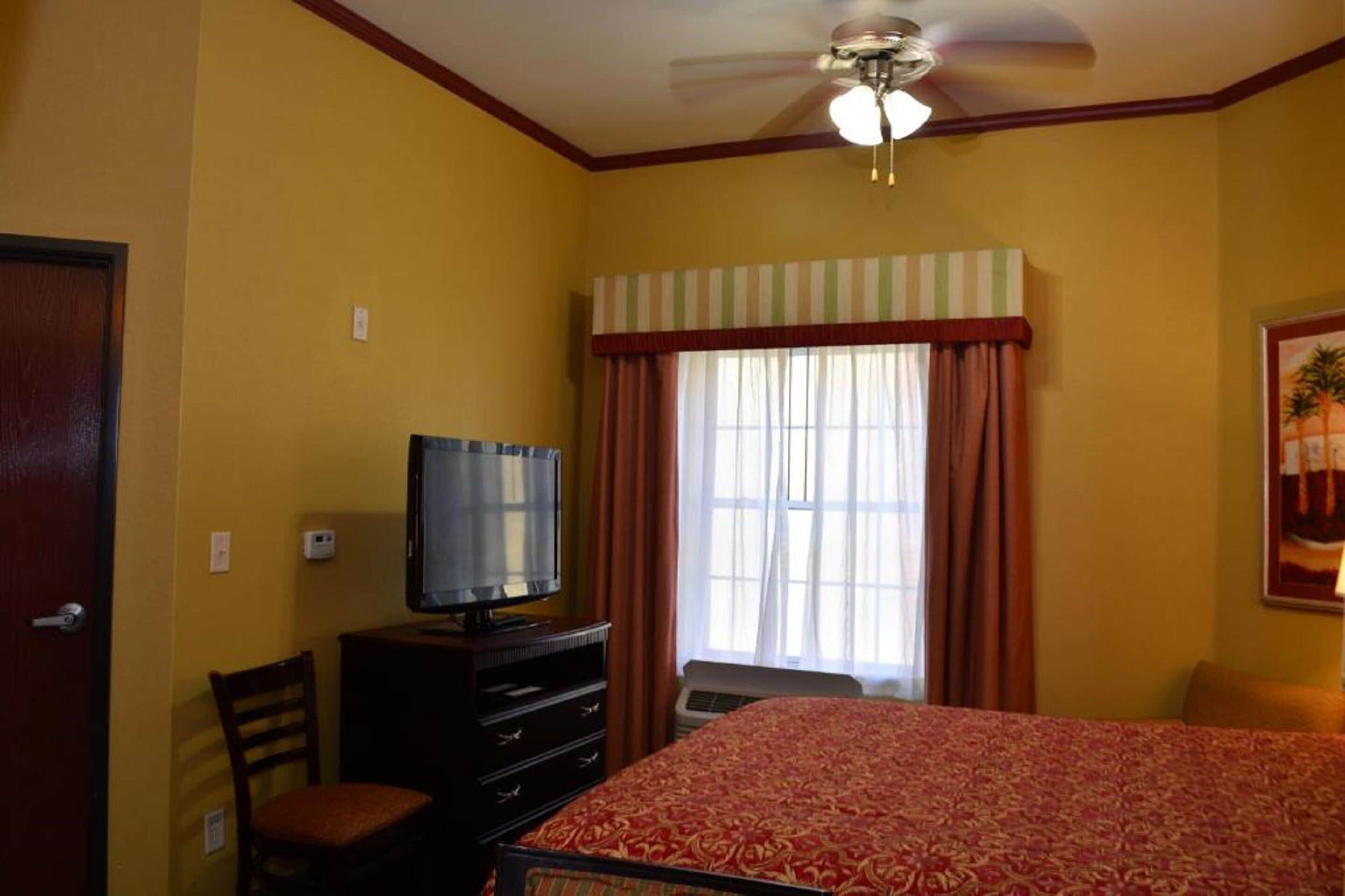 Habitació d'hotel amb llit, televisió, cadira, escriptori i finestra amb cortines.