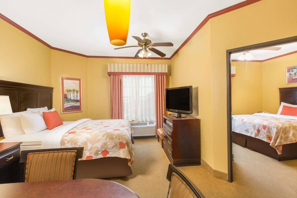 A hotel room with two beds, a television, a desk, and a chair.