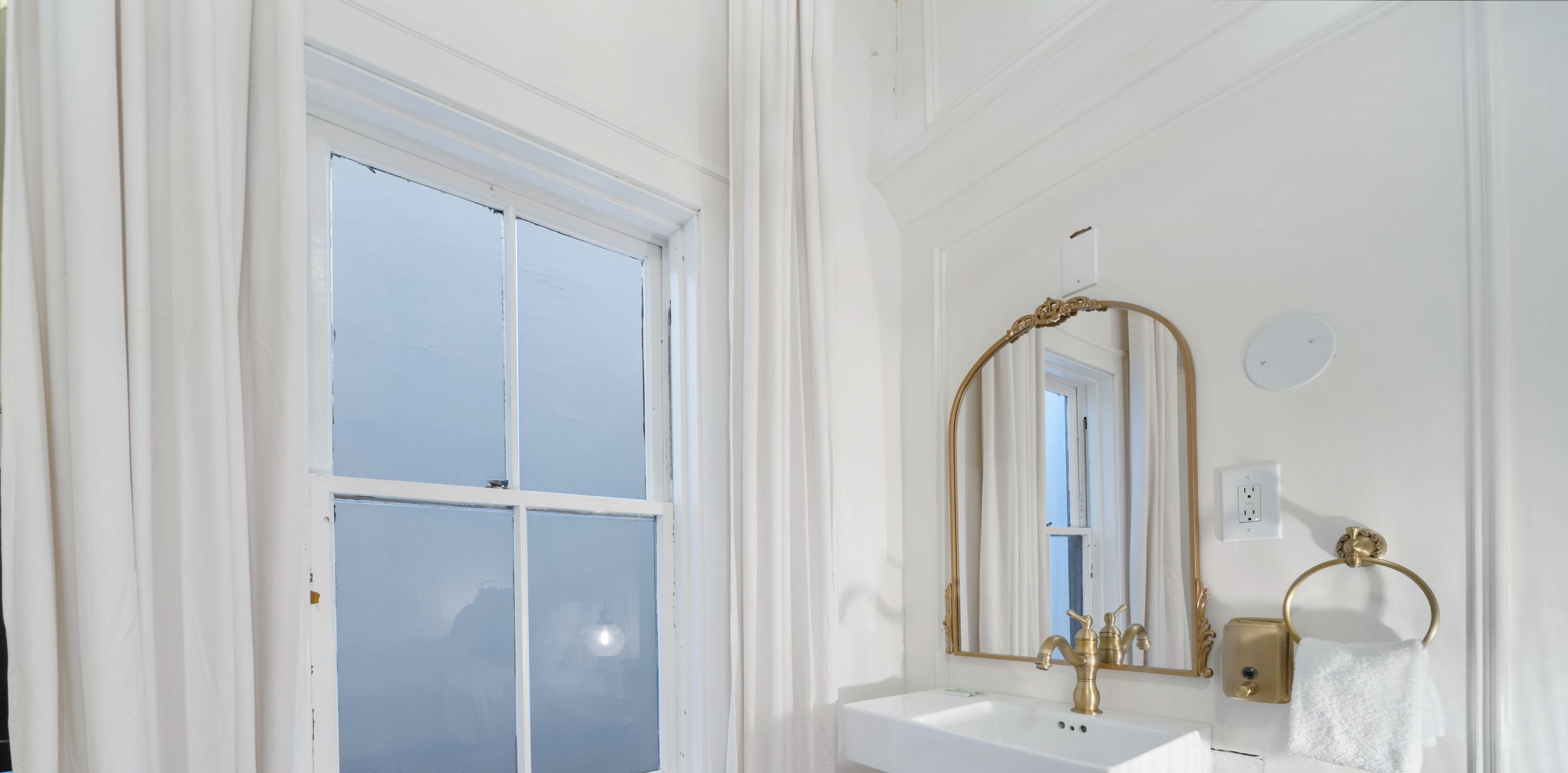 Een badkamer met een wit wastafelmeubel, gouden kranen en een grote spiegel met een sierlijk omlijsting.