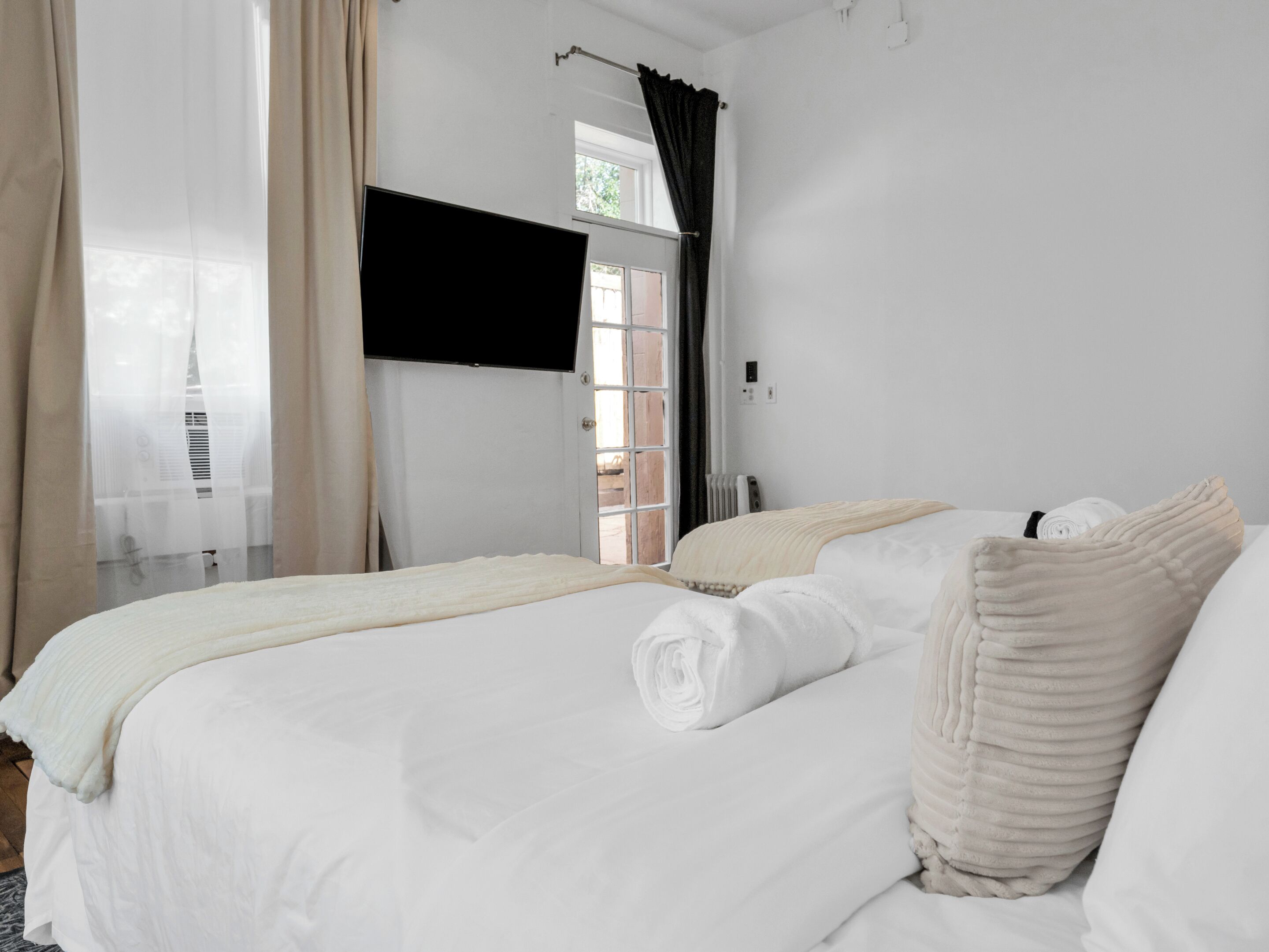 A hotel room with a bed, a window with curtains, a radiator, and a television on the wall.