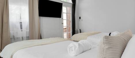 A hotel room with a bed, a window with curtains, a radiator, and a television on the wall.