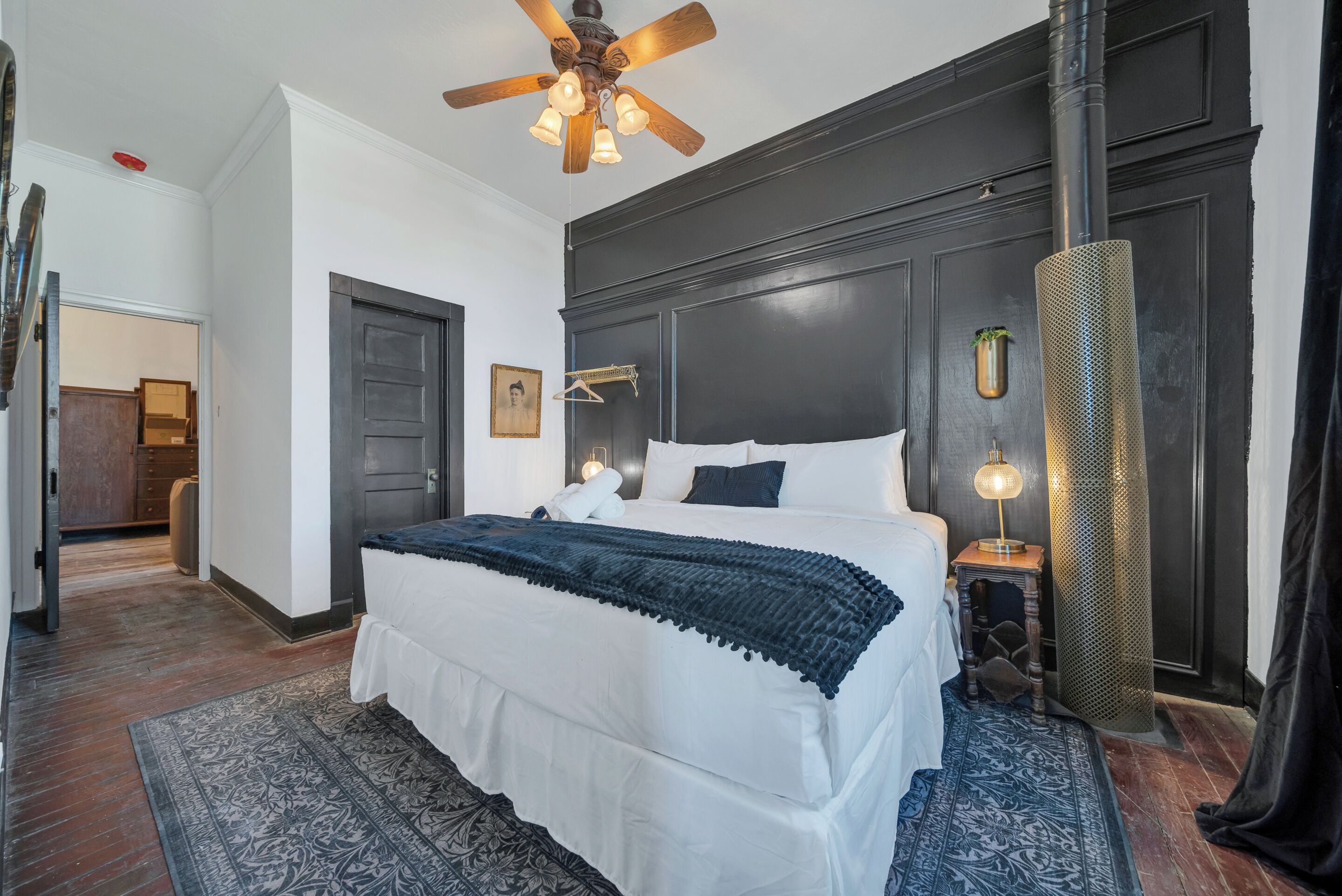 Une chambre à coucher avec un grand lit, un ventilateur de plafond, une table de chevet avec une lampe et une tête de lit en bois foncé.