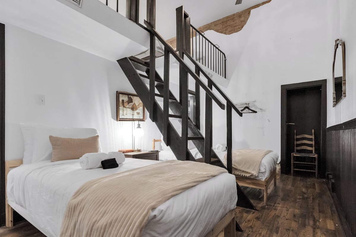 Une chambre avec un escalier en bois, un lit avec une literie blanche, une table de chevet et une chaise.