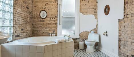 A bathroom with a bathtub, toilet, and a window with a mirror.