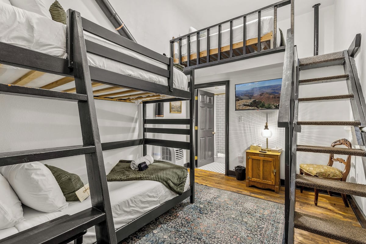 Une chambre avec un lit superposé, une petite échelle en bois, une petite armoire en bois et une chaise.