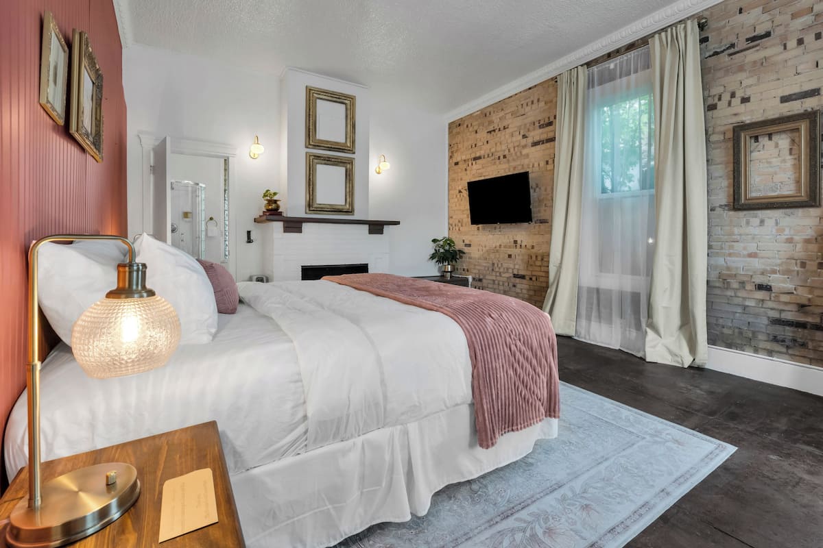 Une chambre moderne avec un grand lit, une cheminée, une télévision et un mur d’accent en briques.