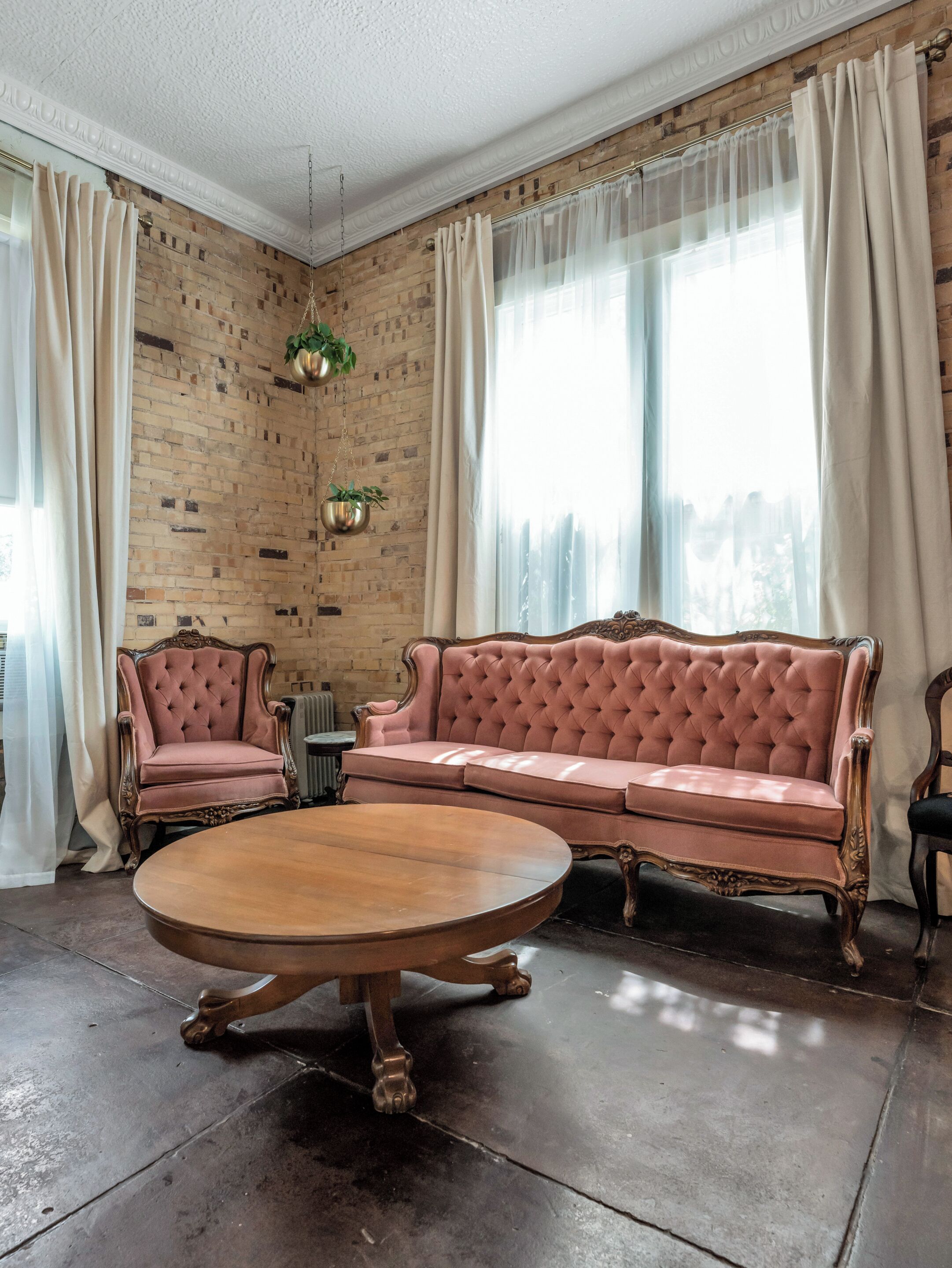 Una habitación con pared de ladrillo, un sofá rosa, una mesa redonda de madera y un radiador.