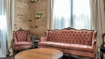 Una habitación con pared de ladrillo, un sofá rosa, una mesa redonda de madera y un radiador.