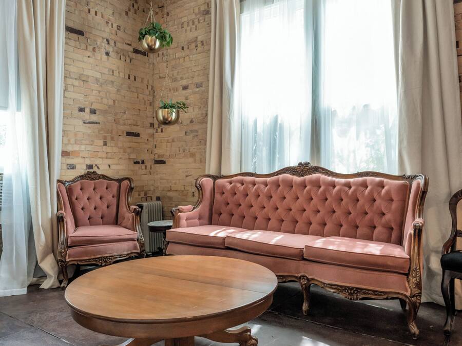 Una habitación con pared de ladrillo, un sofá rosa, una mesa redonda de madera y un radiador.
