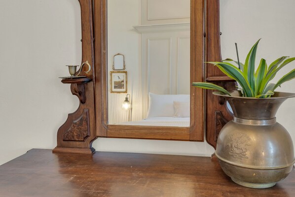 Una mesa de madera con un florero metálico y un espejo enmarco.