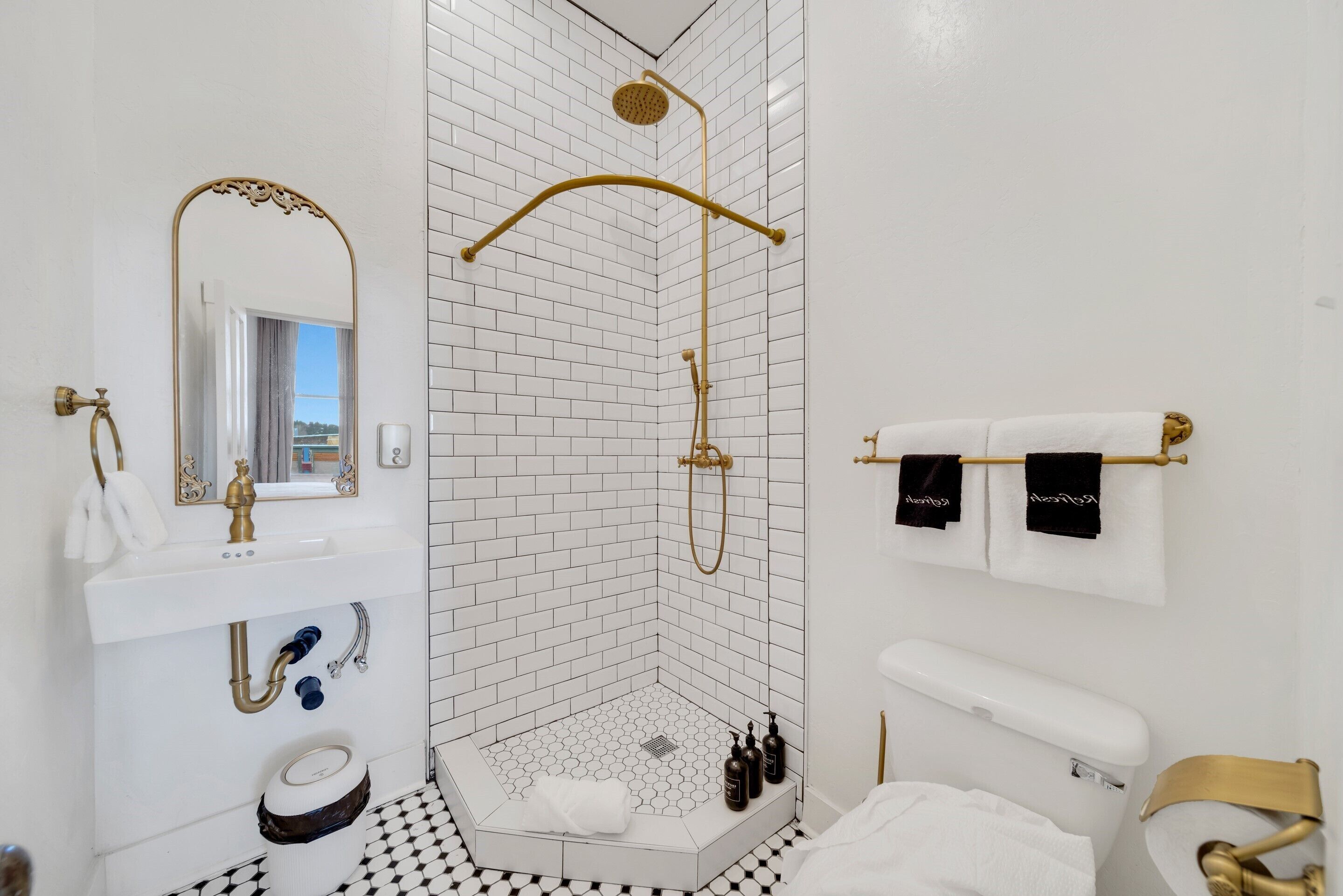 A modern bathroom with a white and black checkered floor, a gold showerhead, and a white sink with a gold faucet.