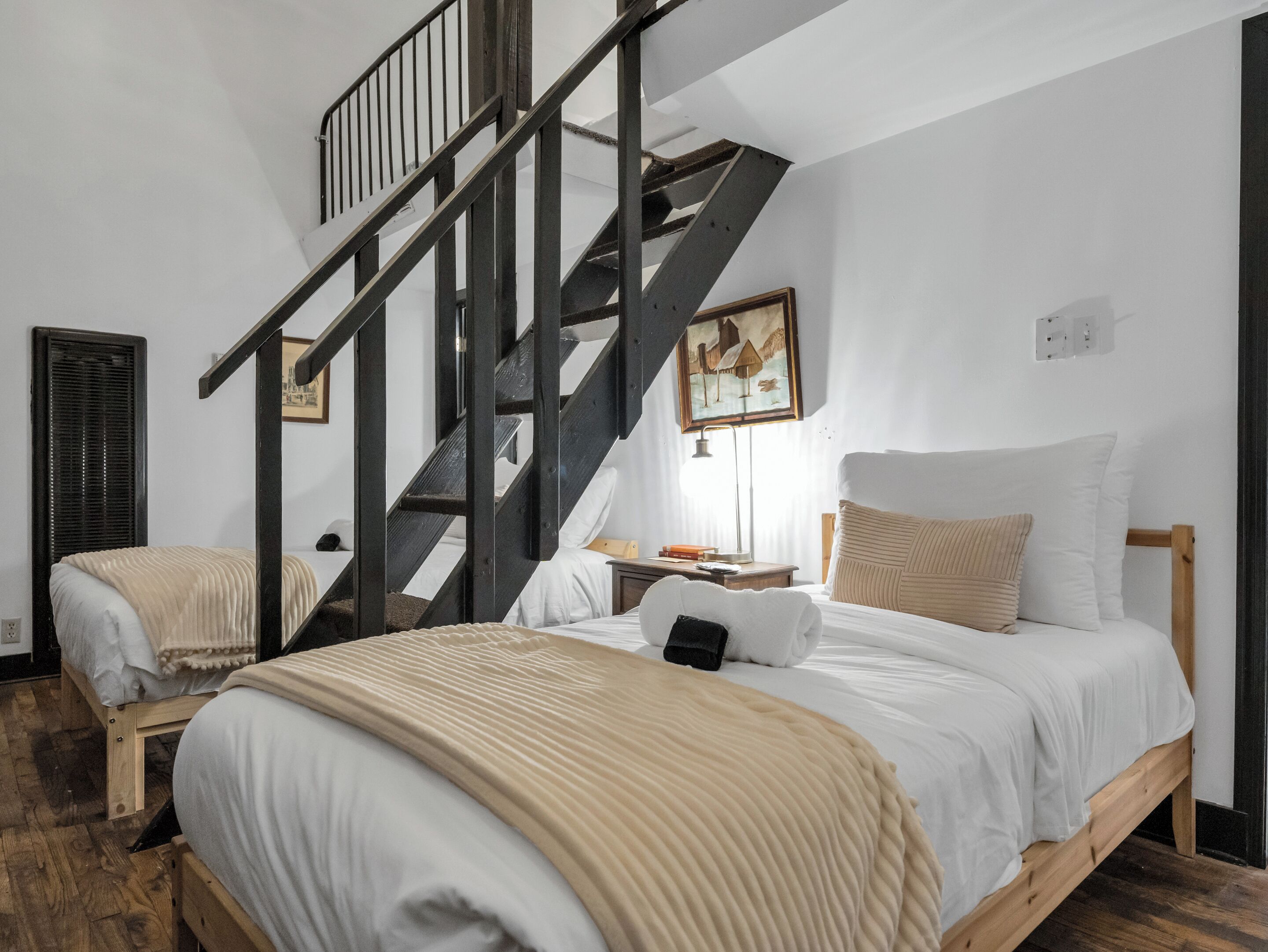 Ein Schlafzimmer mit zwei Betten, einer Holztreppe und einem Gemälde an der Wand.