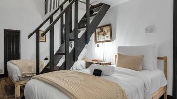 A bedroom with two beds, a wooden staircase, and a painting on the wall.