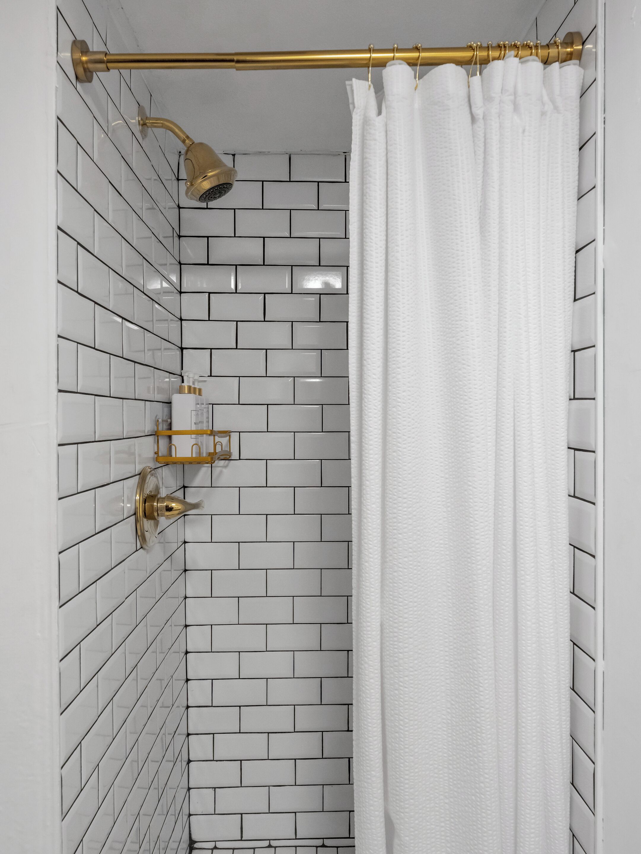 Um chuveiro com paredes revestidas de azulejos brancos e um chuveiro dourado.