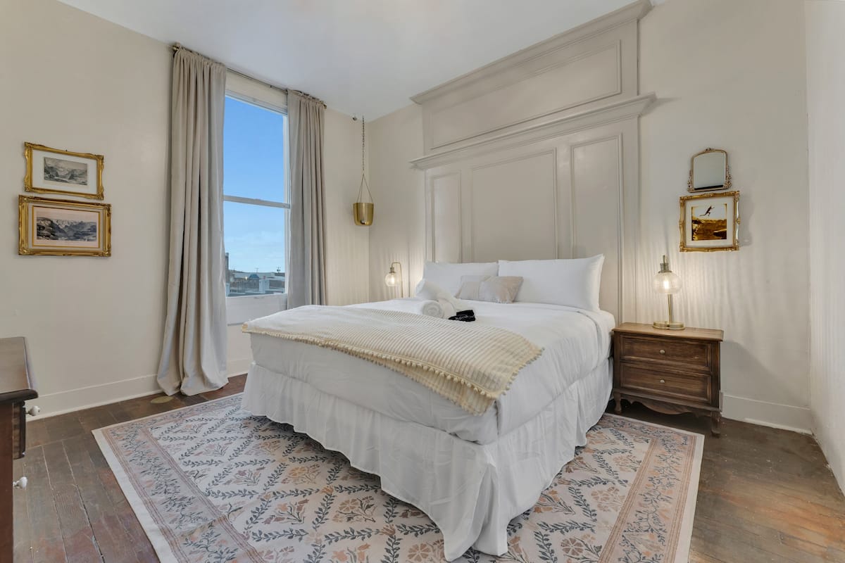 Une chambre avec un grand lit, une table de chevet en bois, une lampe suspendue et une fenêtre avec des rideaux.