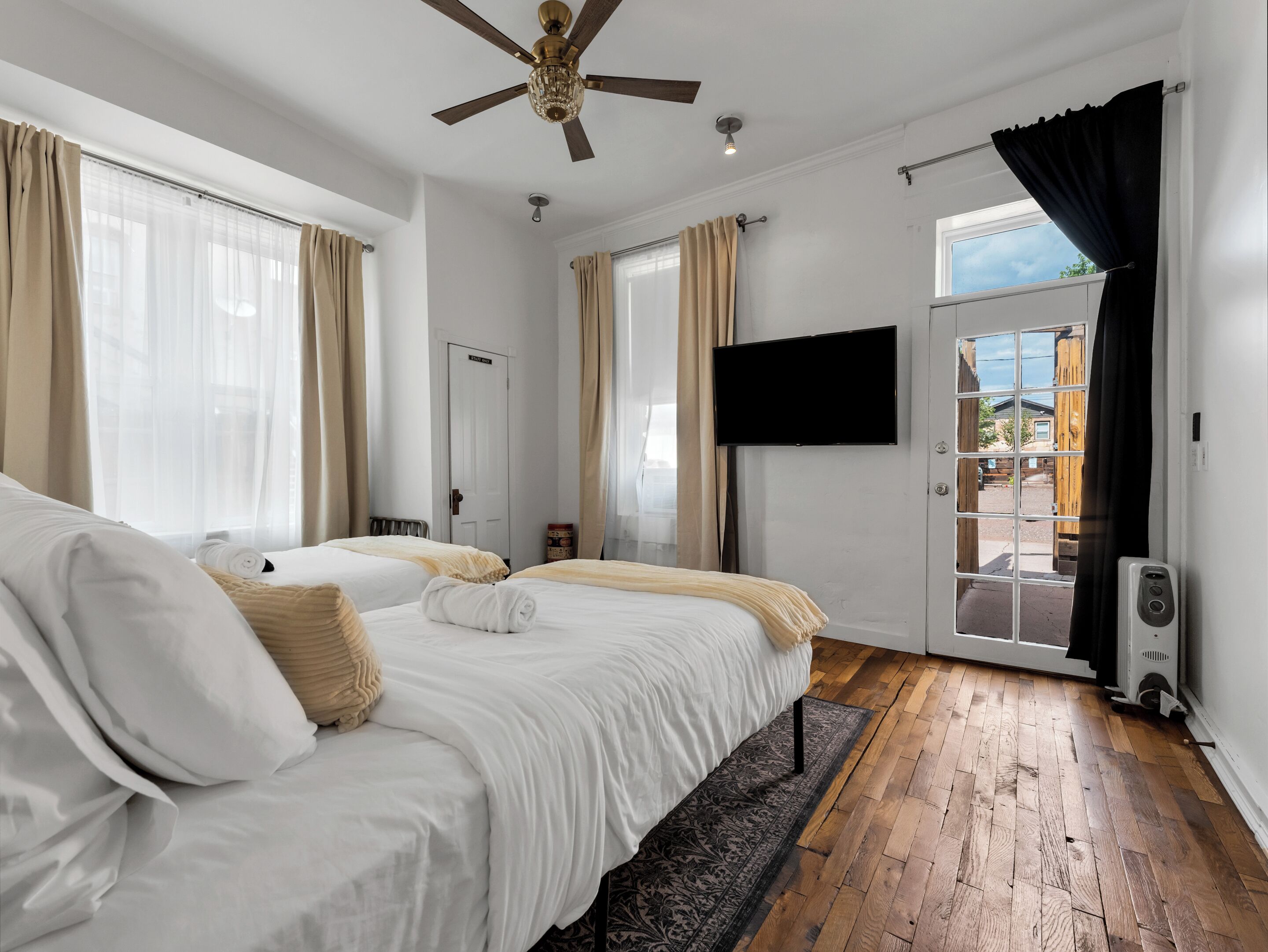Une chambre d’hôtel avec deux lits, un ventilateur de plafond, une télévision et une vue sur l’extérieur.