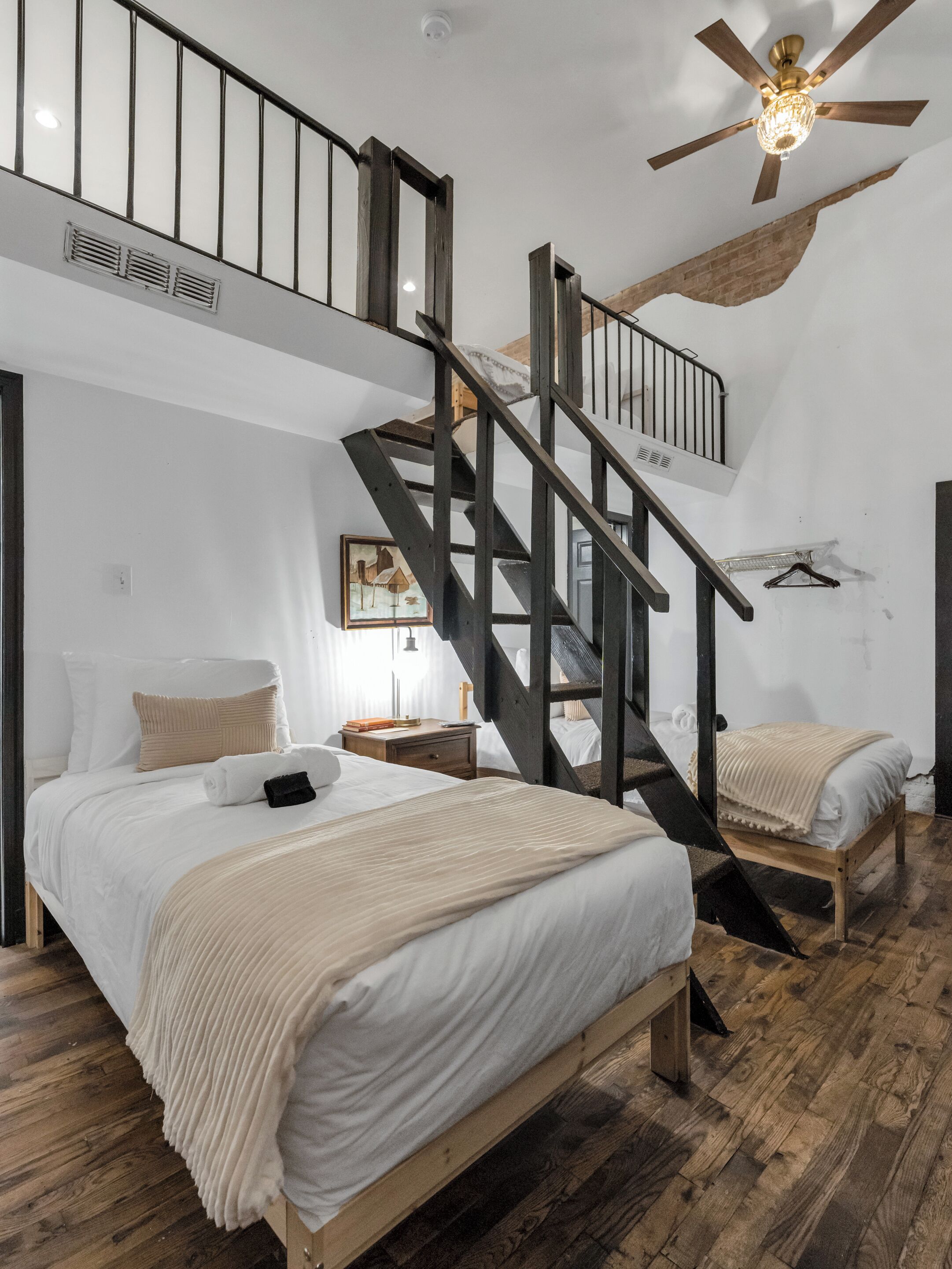 Una camera da letto con una scala in legno, una ventola a soffitto e un letto con copriletto bianco.