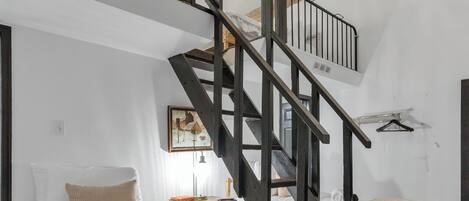 Una camera da letto con una scala in legno, una ventola a soffitto e un letto con copriletto bianco.