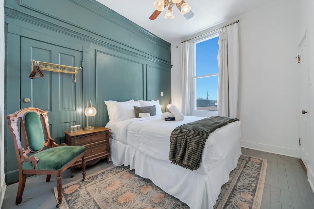 Une chambre à coucher comprenant un lit, une table de chevet, une chaise et une vue sur la ville par une fenêtre.